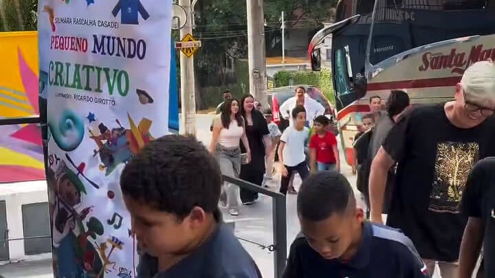 Banner de divulgação do livro O Pequeno Mundo Criativo na entrada do evento de lançamento com chegada do público e crianças.
