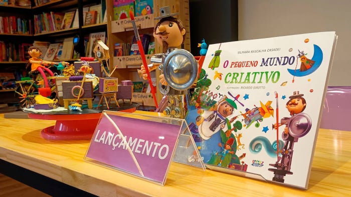 Mesa decorada com brinquedos de material reciclado e o livro O Pequeno Mundo Criativo no evento de lançamento.